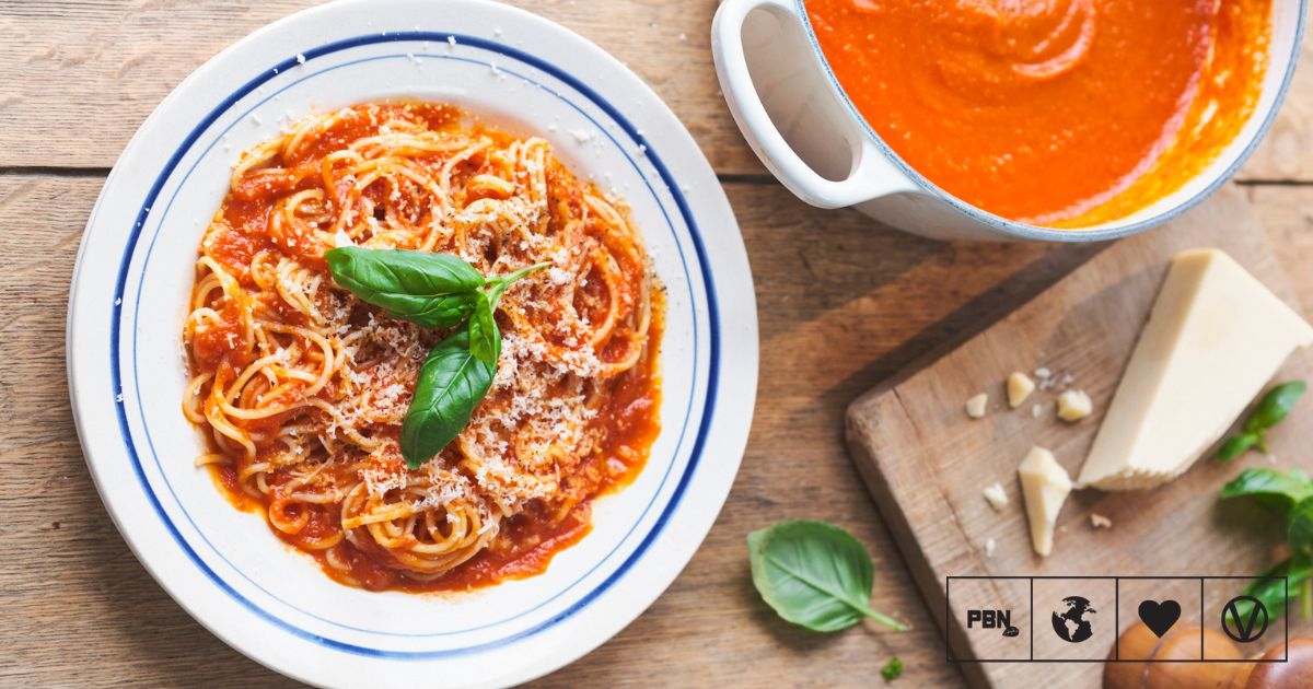 A plate of traditional pasta with a rich red tomato sauce and a sprig of fresh basil on top.