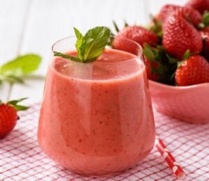 A glass of strawberry juice next to a bowl of strawberries