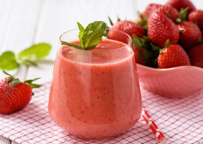 A glass of strawberry juice next to a bowl of strawberries