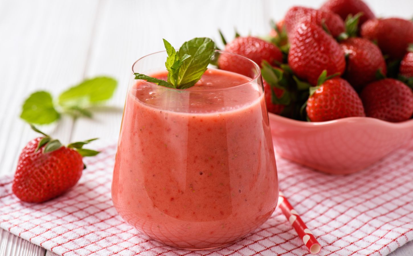 A glass of strawberry juice next to a bowl of strawberries