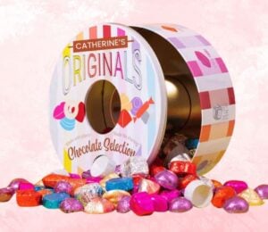 A tin of Catherine's Originals vegan chocolate selection tin in front of a pink background