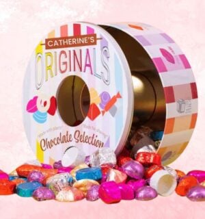 A tin of Catherine's Originals vegan chocolate selection tin in front of a pink background