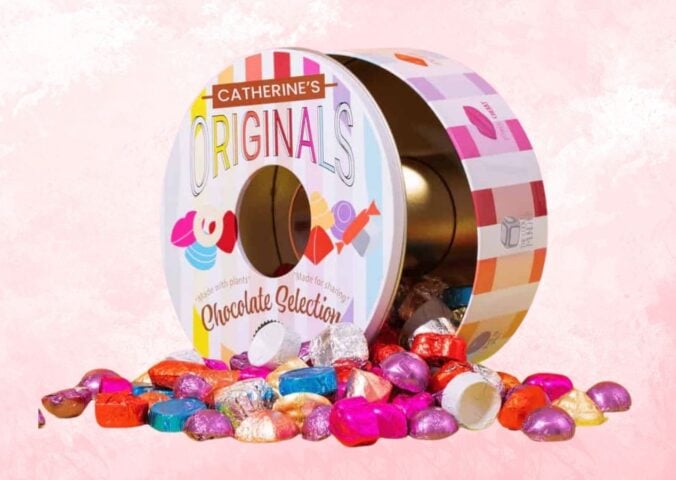 A tin of Catherine's Originals vegan chocolate selection tin in front of a pink background