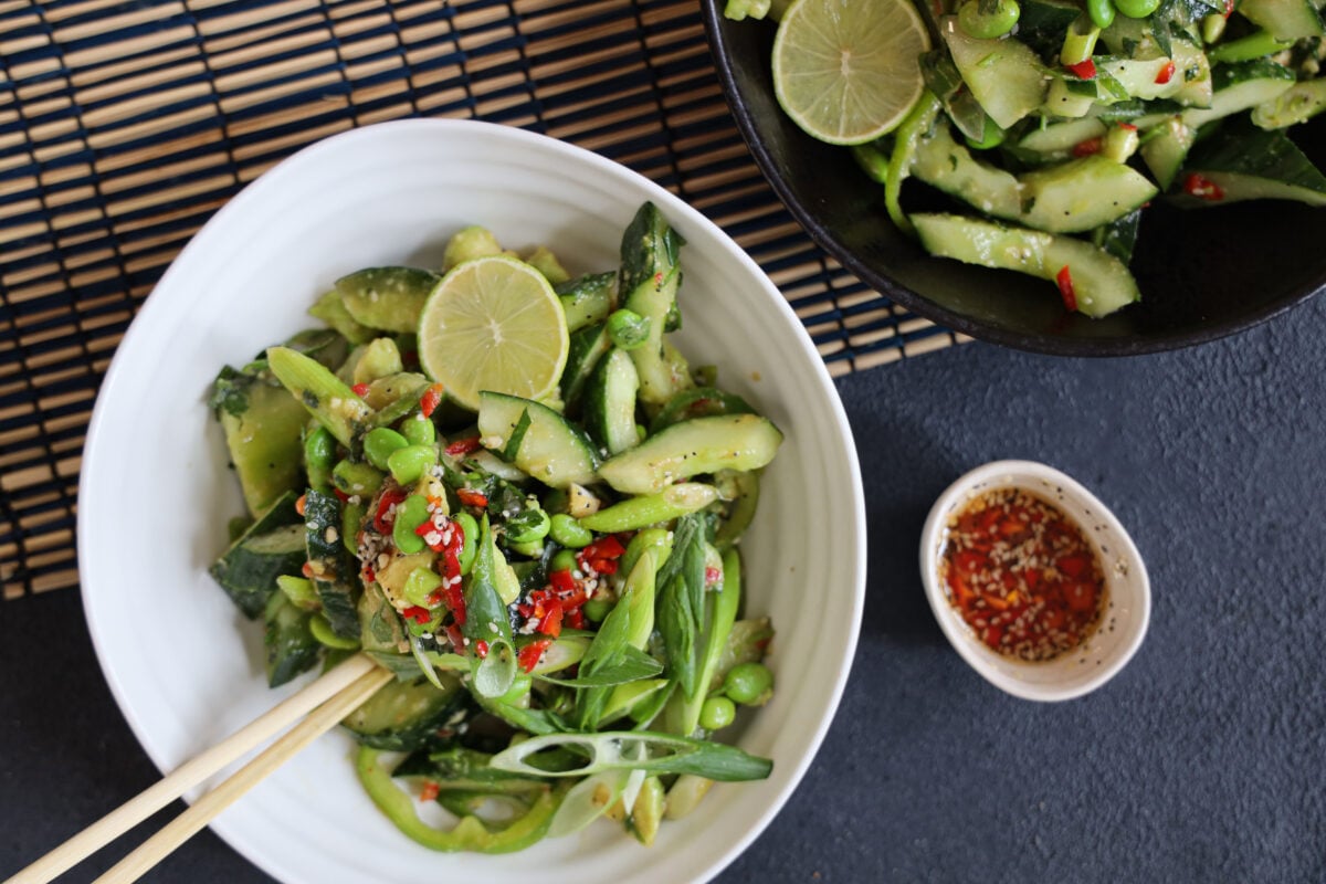 A cucumber salad recipe in a white bowl next to some chili oil 