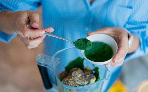 Photo shows someone spooning dark green spirulina into a blender to make smoothies