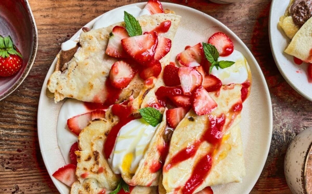 a picture of 4 ingredient vegan crepes covered in strawberries, yogurt, and a berry coulis