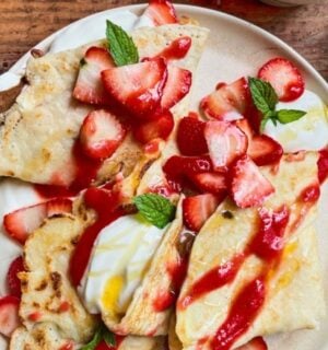 a picture of 4 ingredient vegan crepes covered in strawberries, yogurt, and a berry coulis