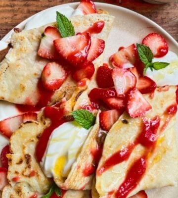 a picture of 4 ingredient vegan crepes covered in strawberries, yogurt, and a berry coulis