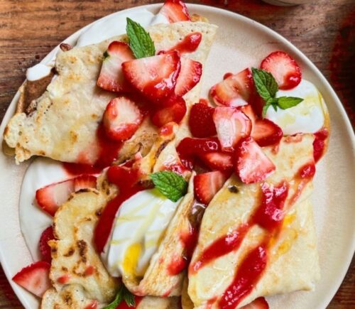 a picture of 4 ingredient vegan crepes covered in strawberries, yogurt, and a berry coulis