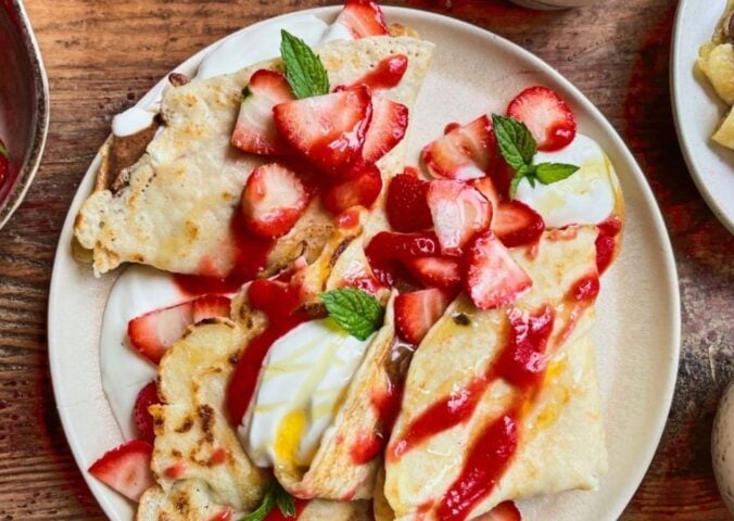 a picture of 4 ingredient vegan crepes covered in strawberries, yogurt, and a berry coulis