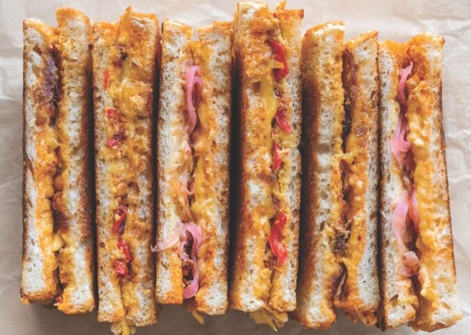 a picture of several vegan grilled cheese sandwiches paired with chili crisp. pickled onions, and more