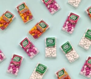 Photo shows a selection of Tic Tac boxes in different flavors and colors on a pale blue background