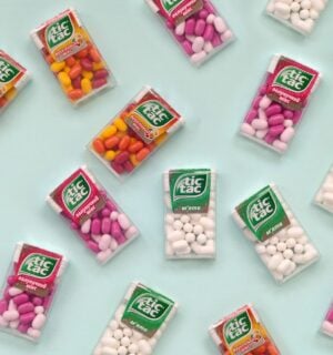 Photo shows a selection of Tic Tac boxes in different flavors and colors on a pale blue background