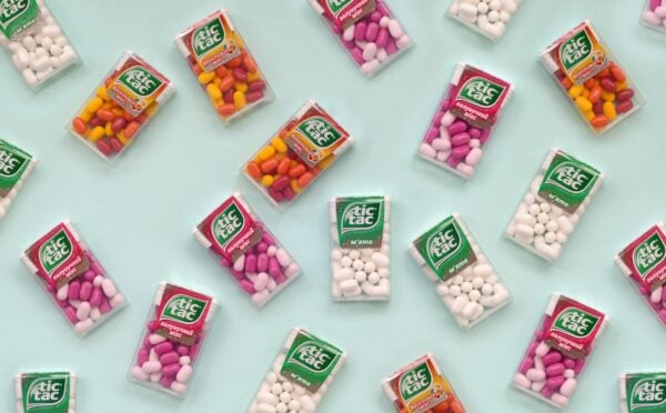 Photo shows a selection of Tic Tac boxes in different flavors and colors on a pale blue background