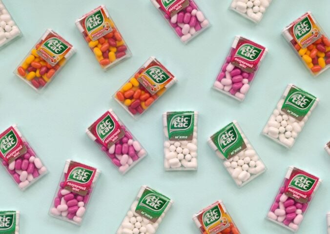 Photo shows a selection of Tic Tac boxes in different flavors and colors on a pale blue background