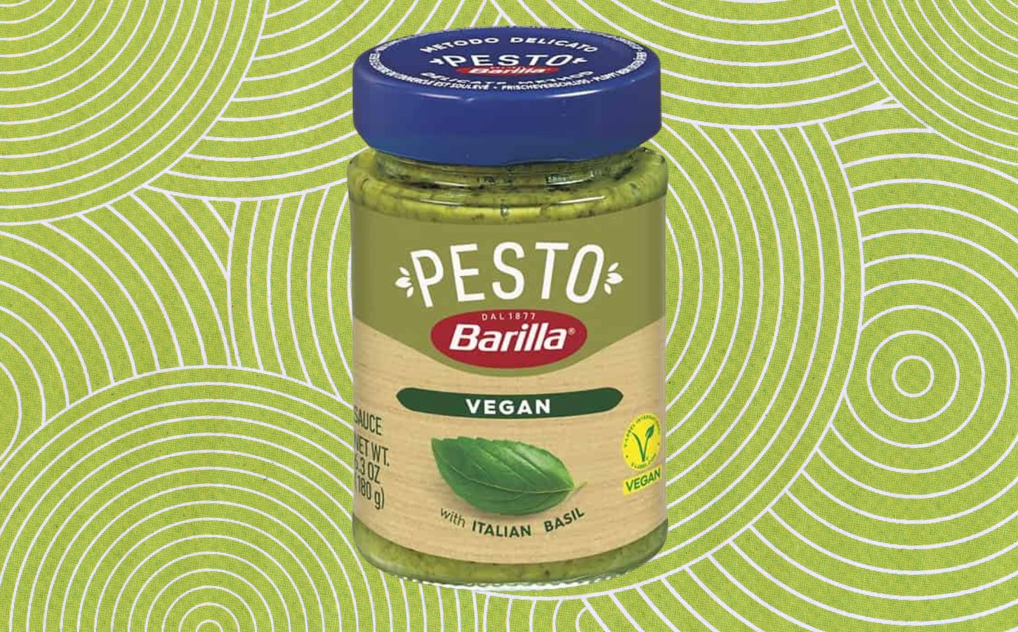 A jar of Barilla vegan pesto in front of a green patterned background