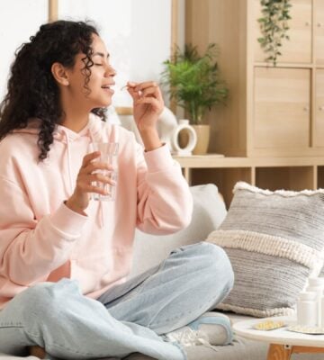 A woman taking supplements in a brightly-lit room while sat on the sofa