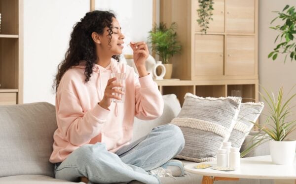 A woman taking supplements in a brightly-lit room while sat on the sofa