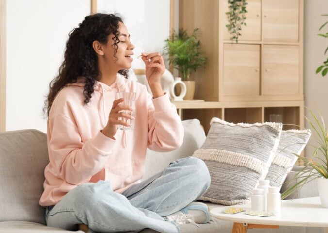 A woman taking supplements in a brightly-lit room while sat on the sofa