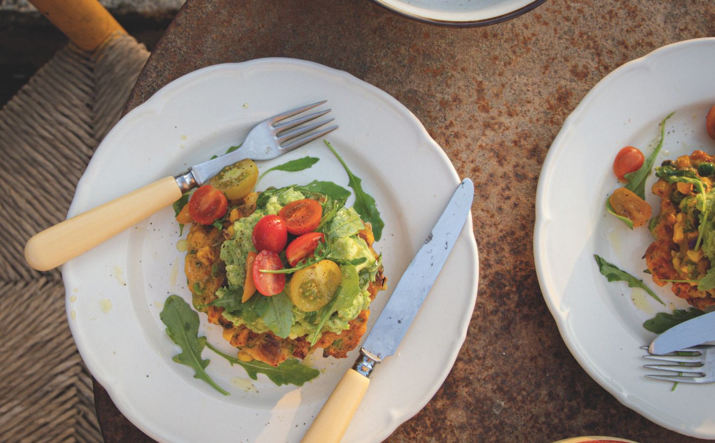 a picture of a corn fritter topped with avocado smash, arugula, and tomato