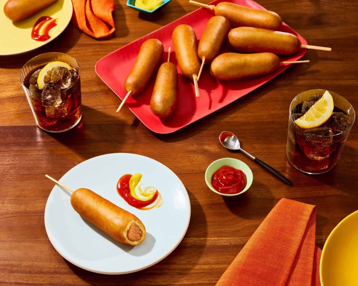 An Impossible Corn Dog on a plate next to soda and ketchup