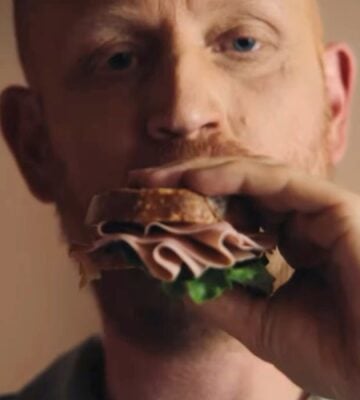 Image is a still taken from La Vie's new TV advertisement, it shows a man taking a bite of a vegan ham sandwich