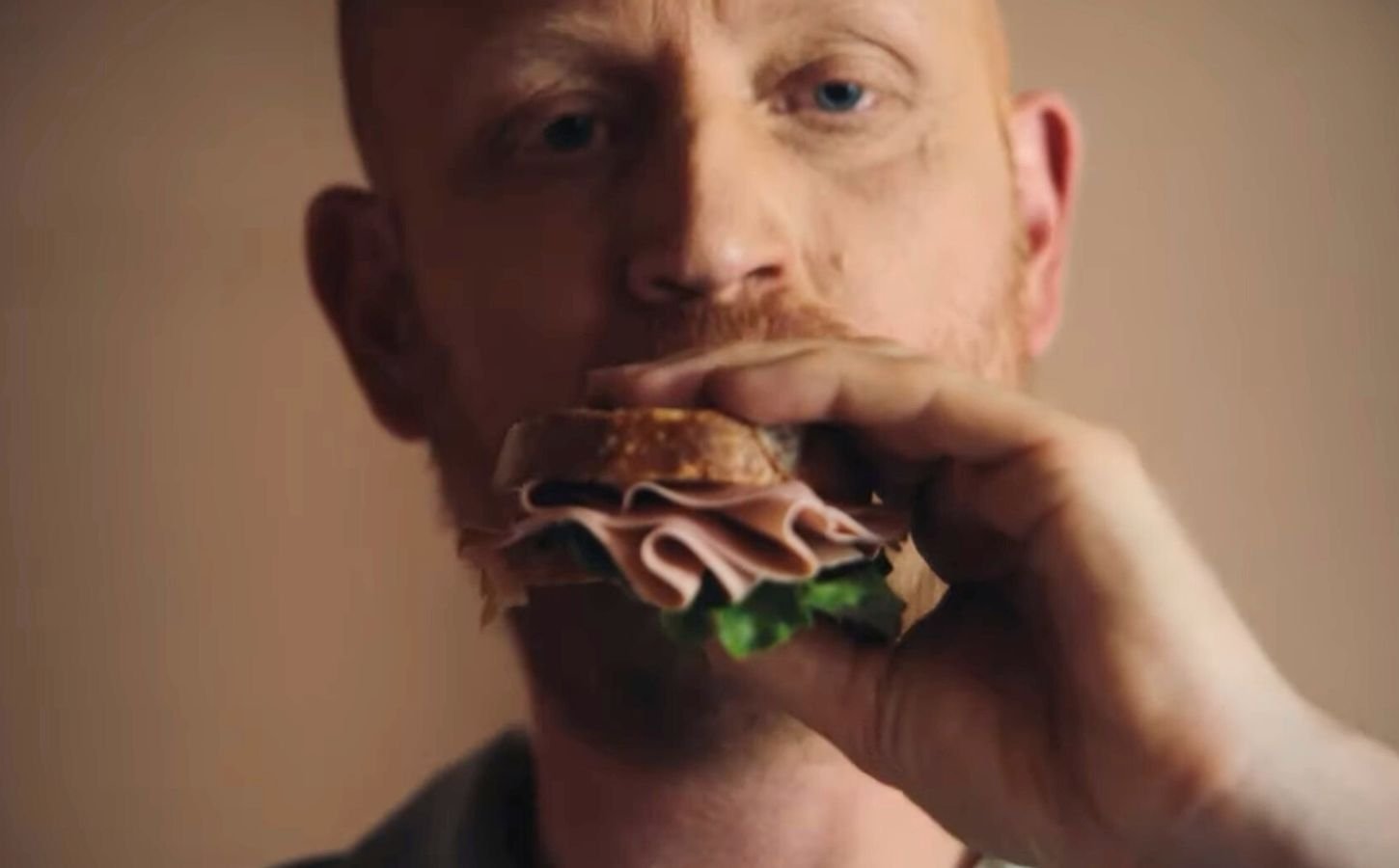 Image is a still taken from La Vie's new TV advertisement, it shows a man taking a bite of a vegan ham sandwich