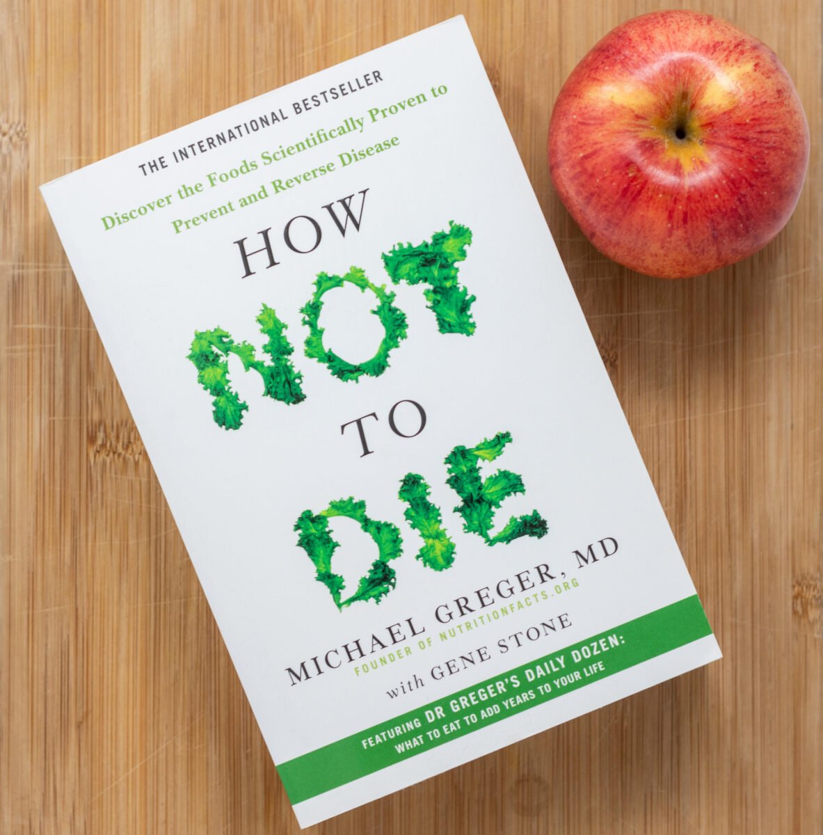 A paperback book of How Not to Die by Michael Greger on a tabletop next to an apple