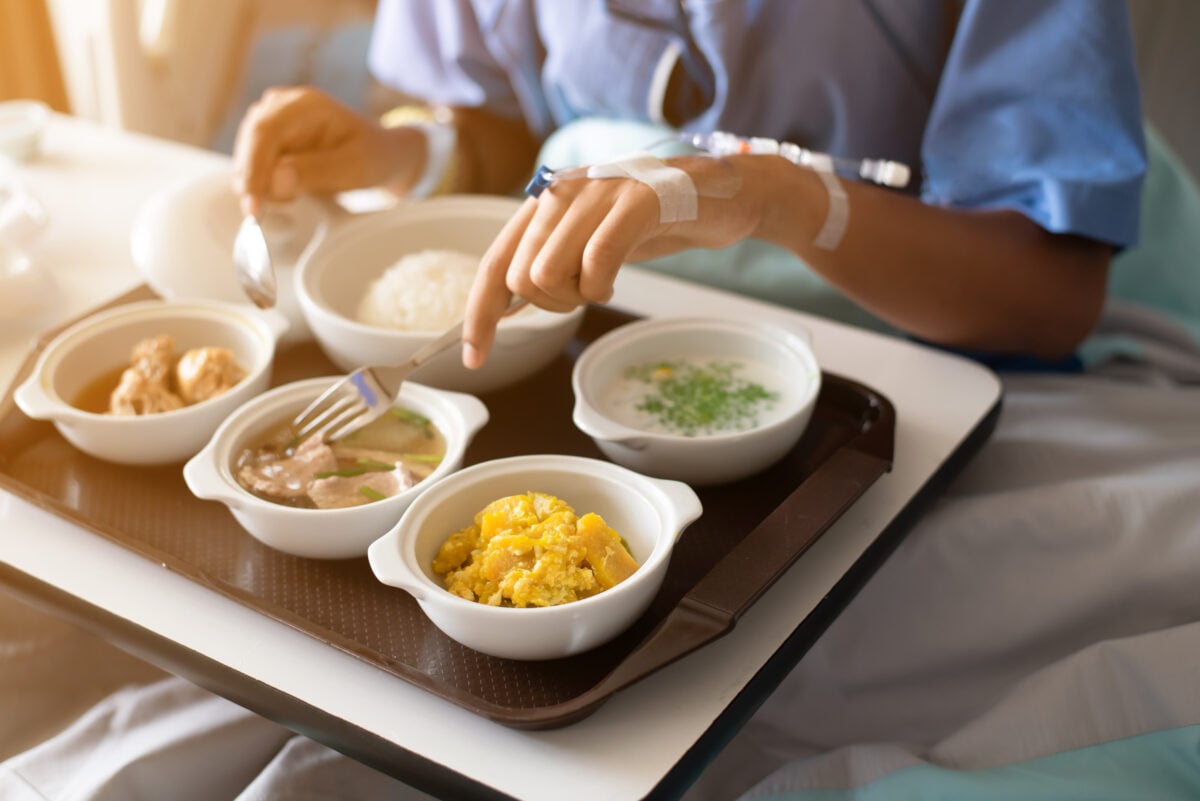 A person eating a selection of meat and other animal products in a hospital bed