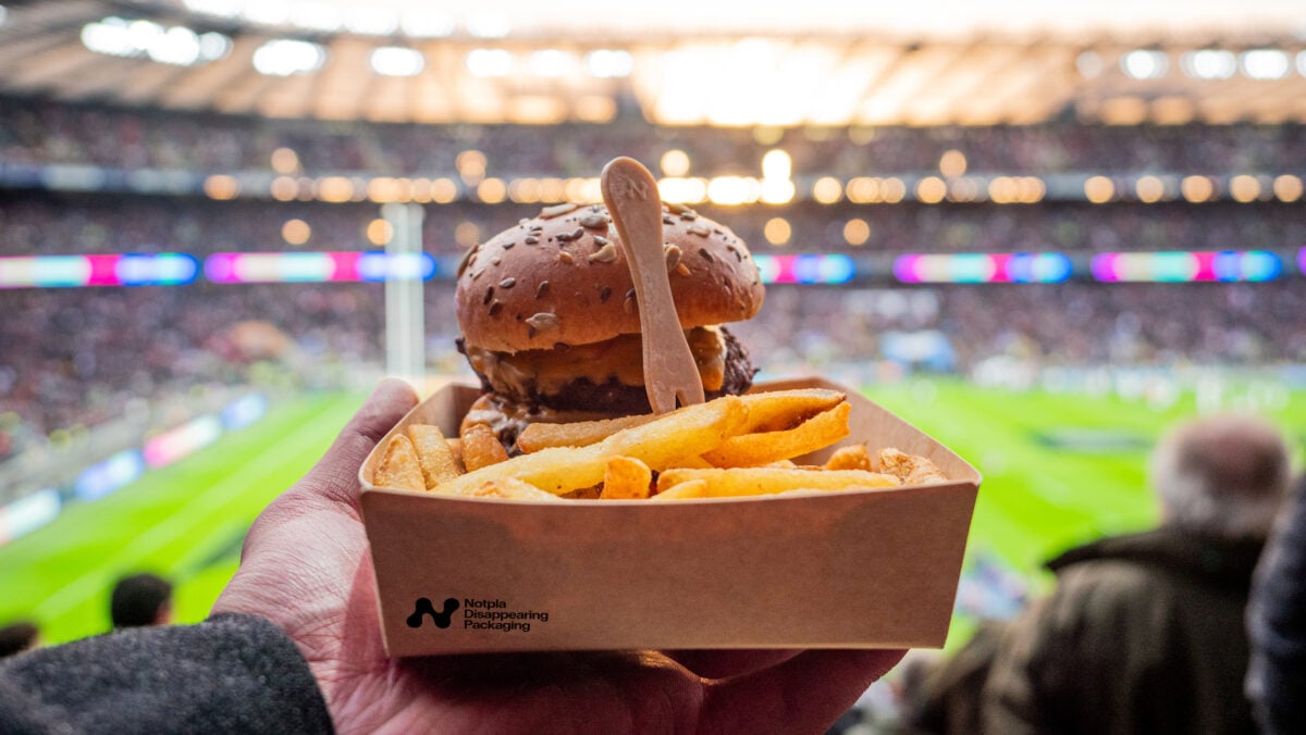 Photo shows a Notpla sustainable packaging box full of fries and a burger at a sports game