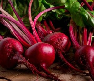 Photo shows a pile of rich purple beets with bright green leaves