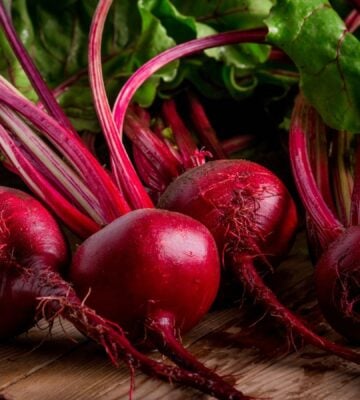 Photo shows a pile of rich purple beets with bright green leaves