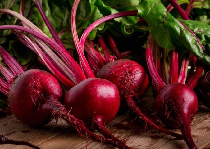 Photo shows a pile of rich purple beets with bright green leaves