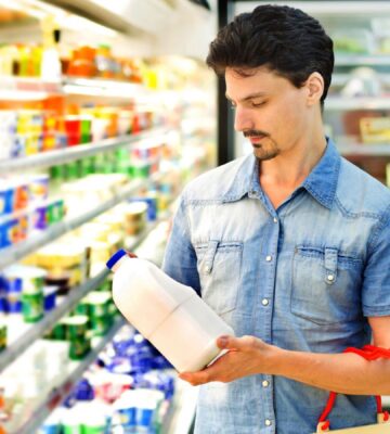 Photo shows holding up a plastic bottle of milk in the refrigerated section of a supermarket