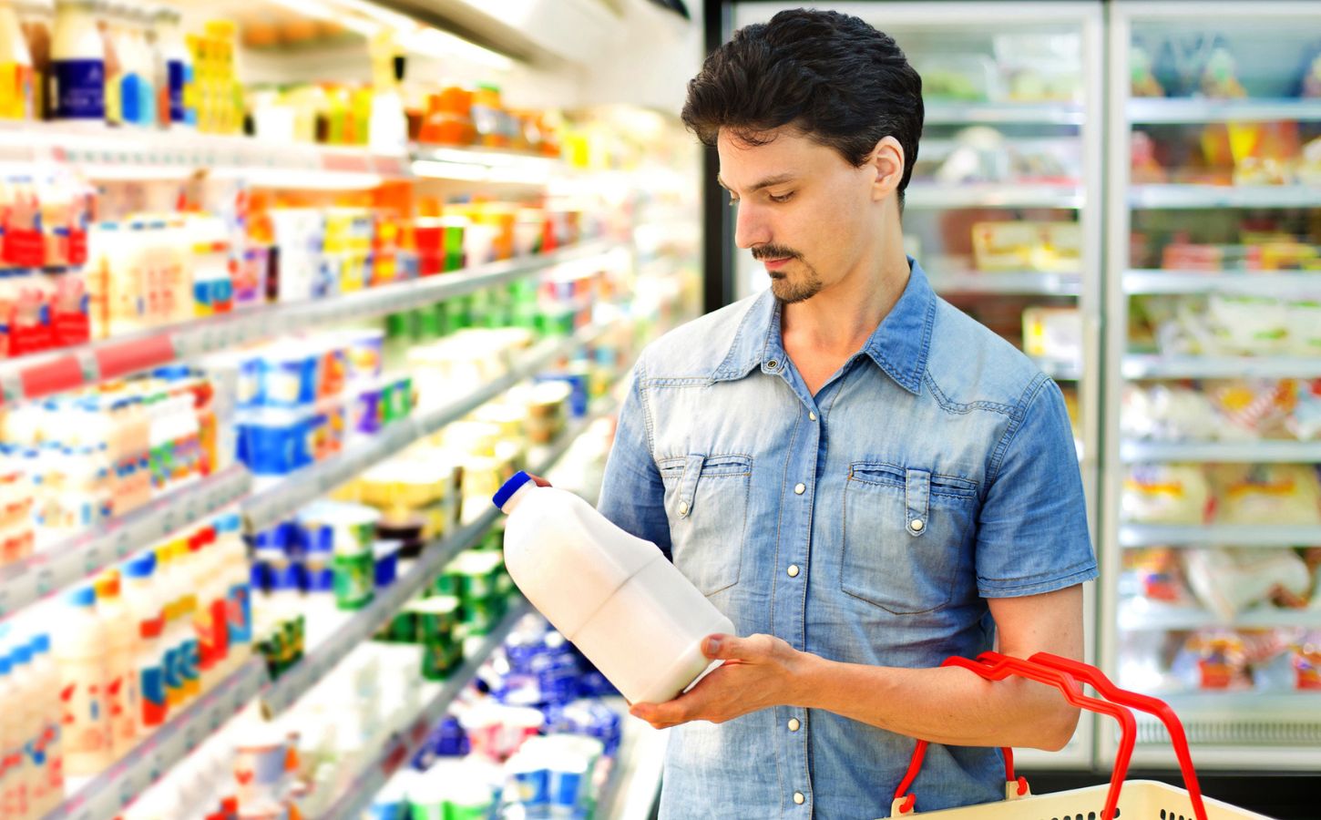 Photo shows holding up a plastic bottle of milk in the refrigerated section of a supermarket