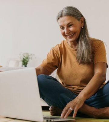 A woman sat on the floor smiling and looking at her laptop