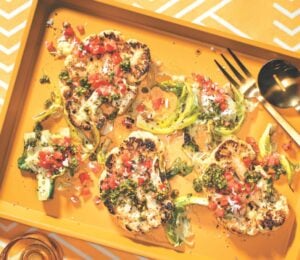 a vibrant picture of spice-rubbed cauliflower steaks on a serving platter with pistachio and cilantro gremolata and tomato and coconut koshumbri