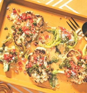 a vibrant picture of spice-rubbed cauliflower steaks on a serving platter with pistachio and cilantro gremolata and tomato and coconut koshumbri