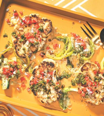 a vibrant picture of spice-rubbed cauliflower steaks on a serving platter with pistachio and cilantro gremolata and tomato and coconut koshumbri