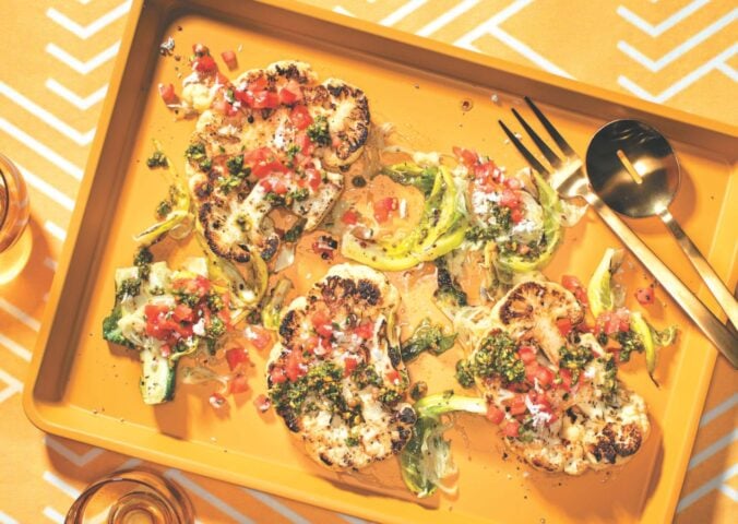 a vibrant picture of spice-rubbed cauliflower steaks on a serving platter with pistachio and cilantro gremolata and tomato and coconut koshumbri