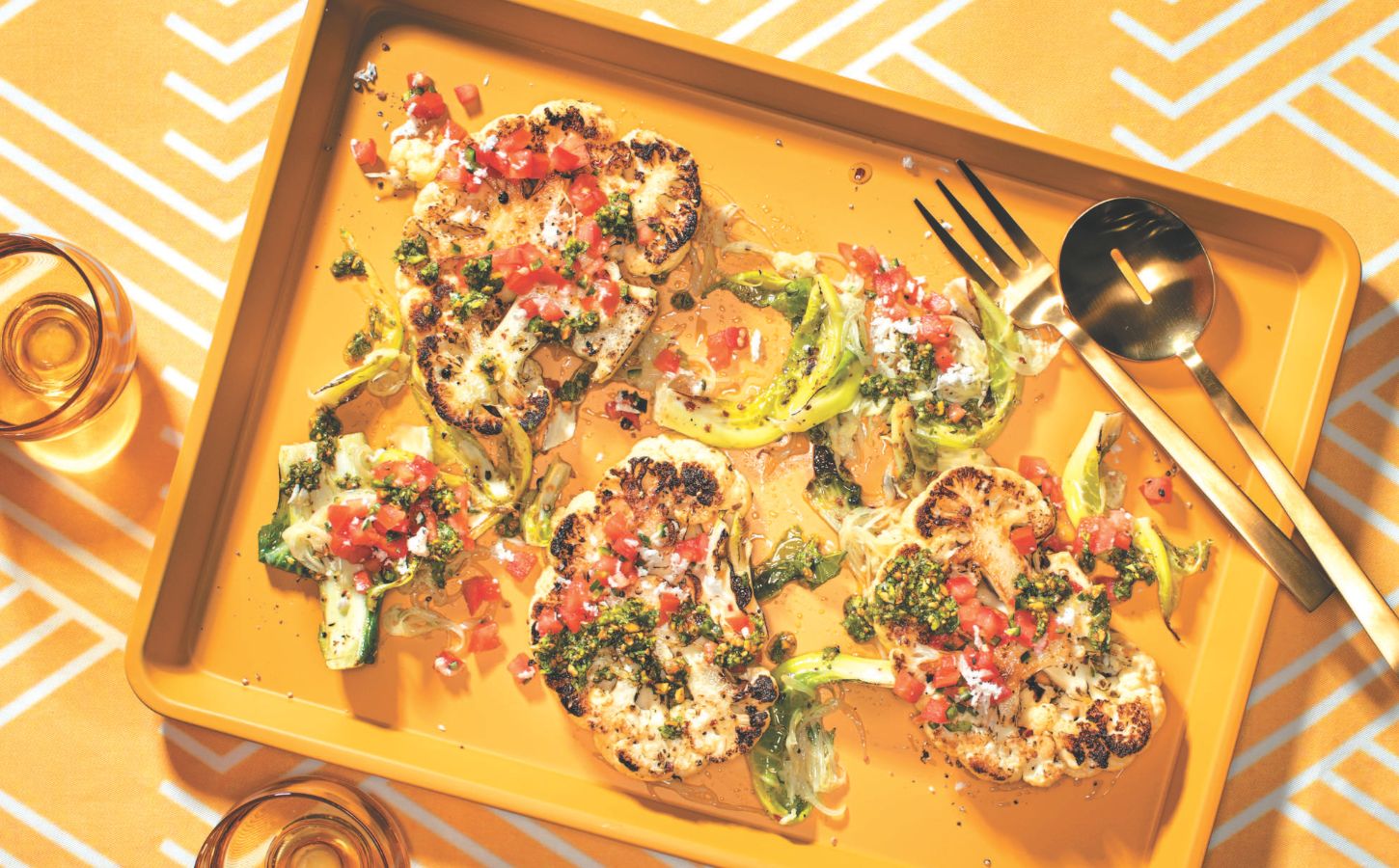 a vibrant picture of spice-rubbed cauliflower steaks on a serving platter with pistachio and cilantro gremolata and tomato and coconut koshumbri