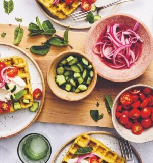 a picture of a table of spiced chickpea waffles with pickled onions, cucumbers, and tomatoes