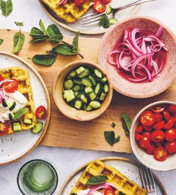 a picture of a table of spiced chickpea waffles with pickled onions, cucumbers, and tomatoes