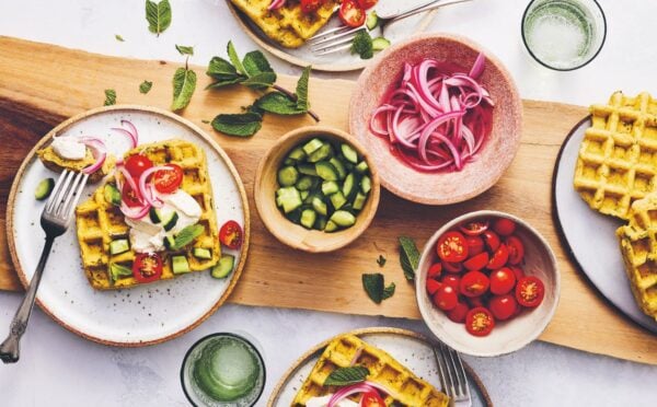 a picture of a table of spiced chickpea waffles with pickled onions, cucumbers, and tomatoes