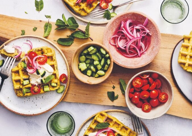 a picture of a table of spiced chickpea waffles with pickled onions, cucumbers, and tomatoes