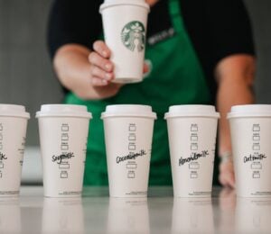 Five Starbucks cups in a row with various names of dairy-free milks written on each of them