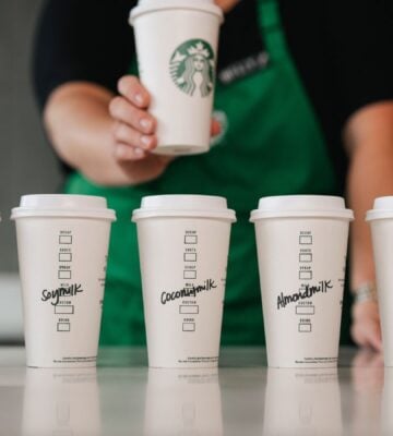 Five Starbucks cups in a row with various names of dairy-free milks written on each of them