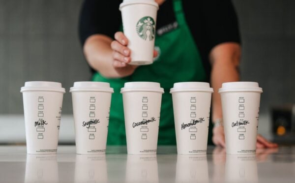 Five Starbucks cups in a row with various names of dairy-free milks written on each of them