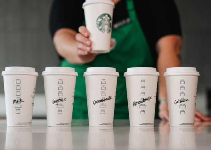 Five Starbucks cups in a row with various names of dairy-free milks written on each of them