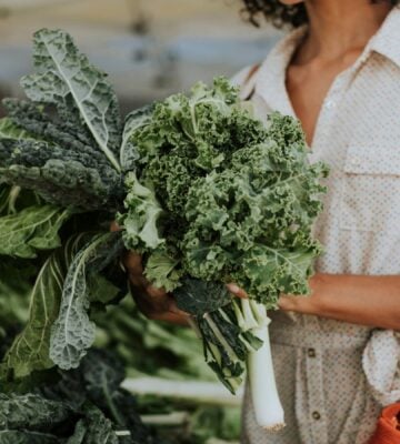 Photo shows a woman shopping and holding a large bunch of fresh kale, which is one of the top sources of plant-based calcium